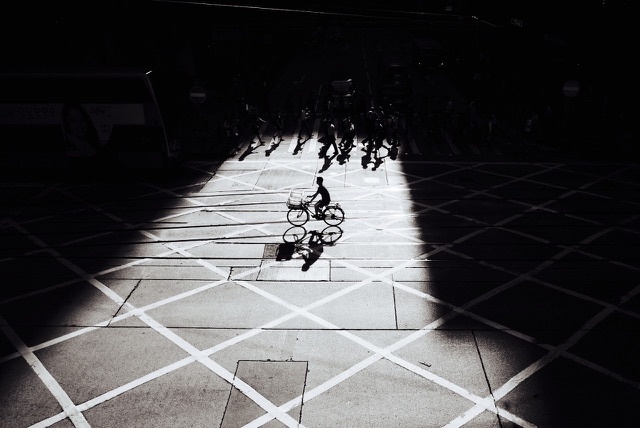 After: Cyclist crossing a sunlit plaza between deep shadows, edited with the free Black & White LUTs