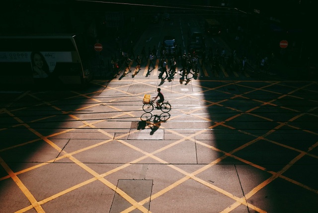 Before: Cyclist crossing a sunlit plaza between deep shadows