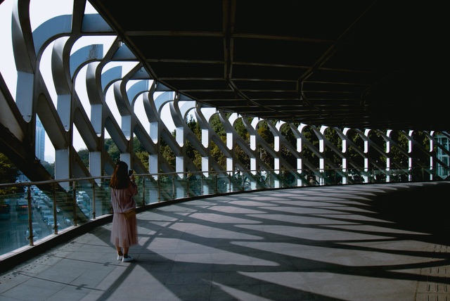 After: Woman walking along a curved pedestrian bridge with patterned shadows, edited with the free Cinematic LUTs