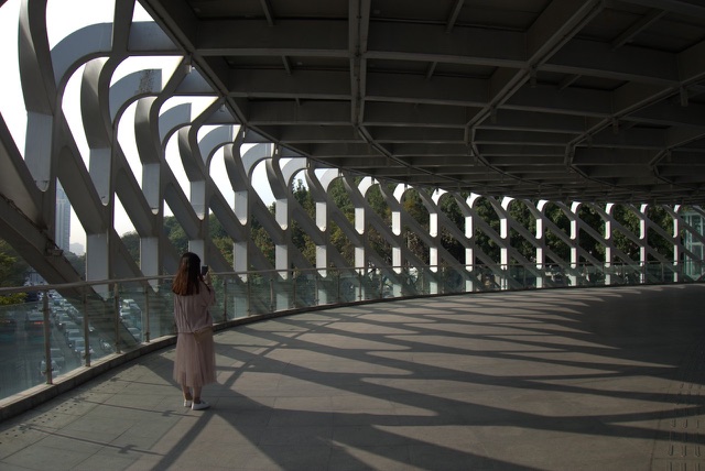 Before: Woman walking along a curved pedestrian bridge with patterned shadows
