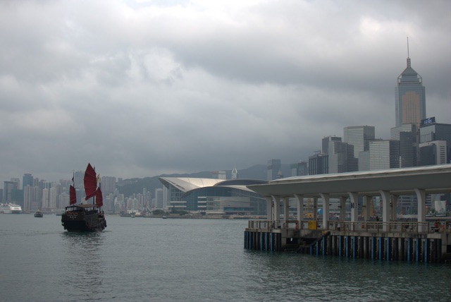 Before: Hong Kong harbor with a red-sailed junk boat and the city skyline