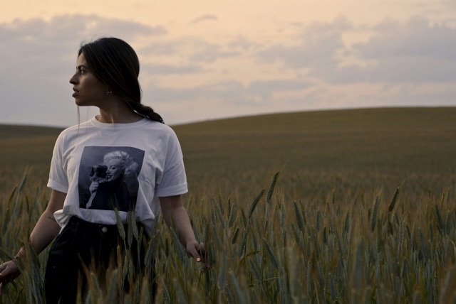Before: Young woman standing in a wheat field at dusk