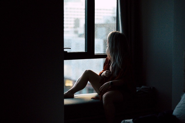 After: Woman sitting by a window in a dim room looking out at the city, edited with the free Moody LUTs
