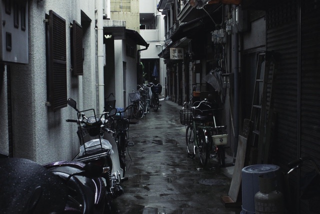 After: Narrow city alley lined with parked bicycles and scooters on a rainy day, edited with the free Moody LUTs