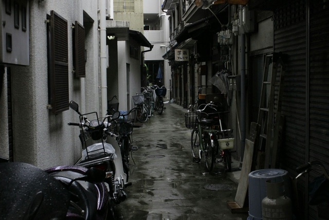Before: Narrow city alley lined with parked bicycles and scooters on a rainy day