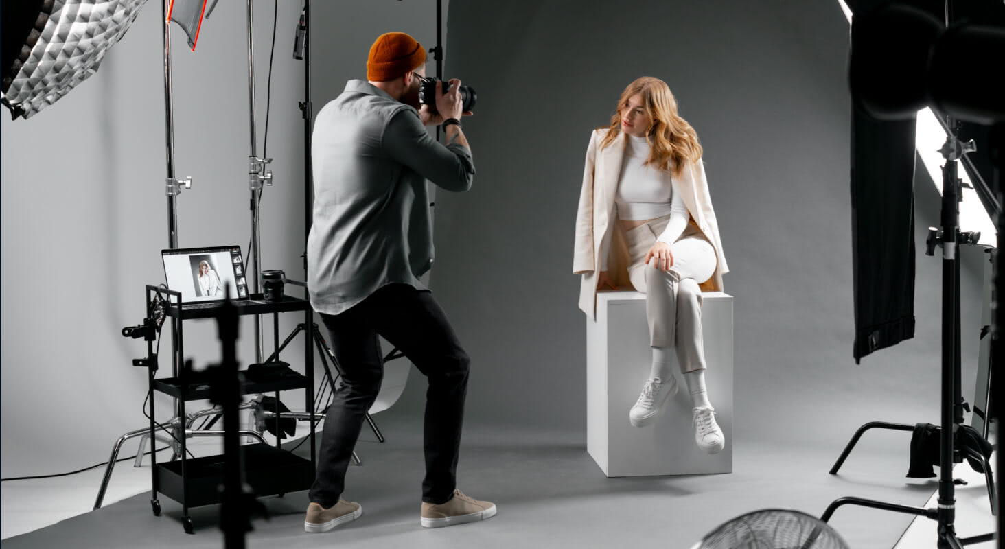 Photographer shooting stylish model under professional studio lights