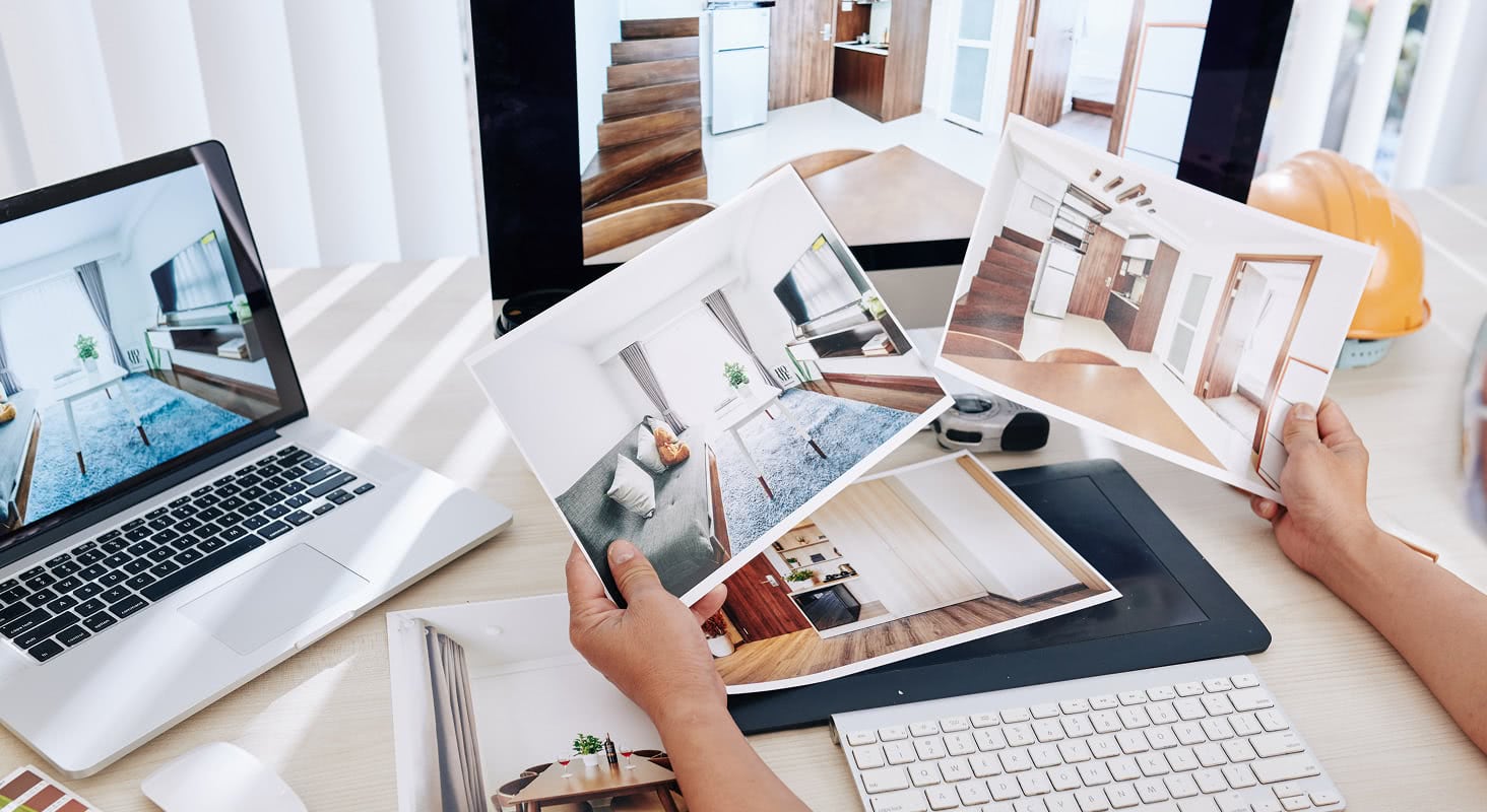 BPhotographer reviewing printed real estate interior photos at a desk with a laptop and editing tablet